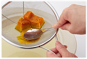チンしたかぼちゃのうち、70gをかぼちゃボール用にとりわけ、残りをざるなどを使って簡単に裏ごししながら、スープを入れた土鍋に溶かし入れます。（ブレンダーやミキサーを使用してもOK）